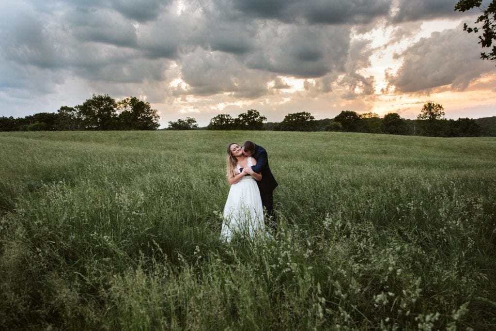 bride and groom in field at sycamore creek family ranch in branson missouri